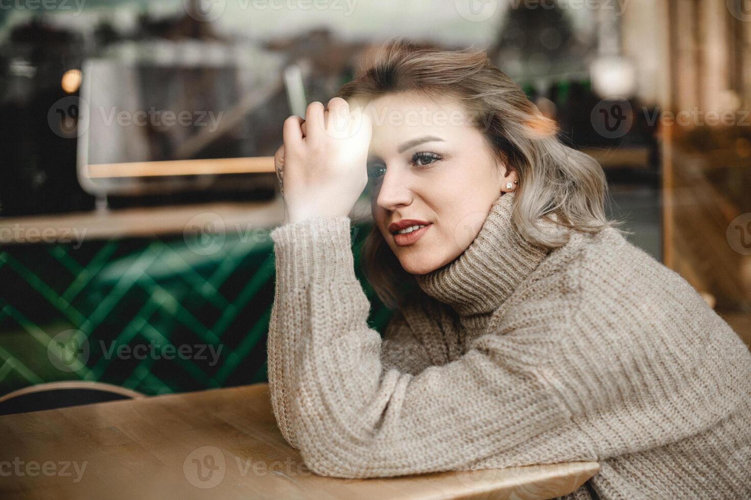 Woman Relaxing at Cafe Table with Joyful Expression. Woman sitting at a table with hands on her head, smiling warmly. Ideal for portraying relaxation, contentment, and casual cafe vibes in a cozy photo
