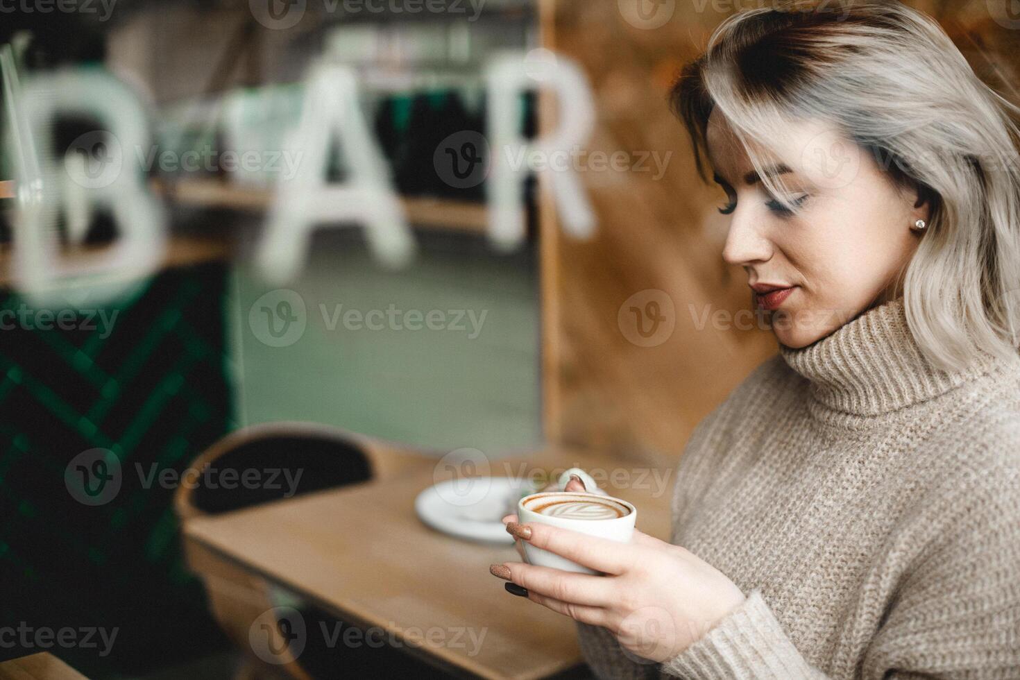 Woman Enjoying Coffee in Cozy Cafe. Woman sipping coffee at a cafe table, surrounded by a warm, inviting atmosphere. Ideal for images of casual cafe life, relaxation, and enjoying coffee photo