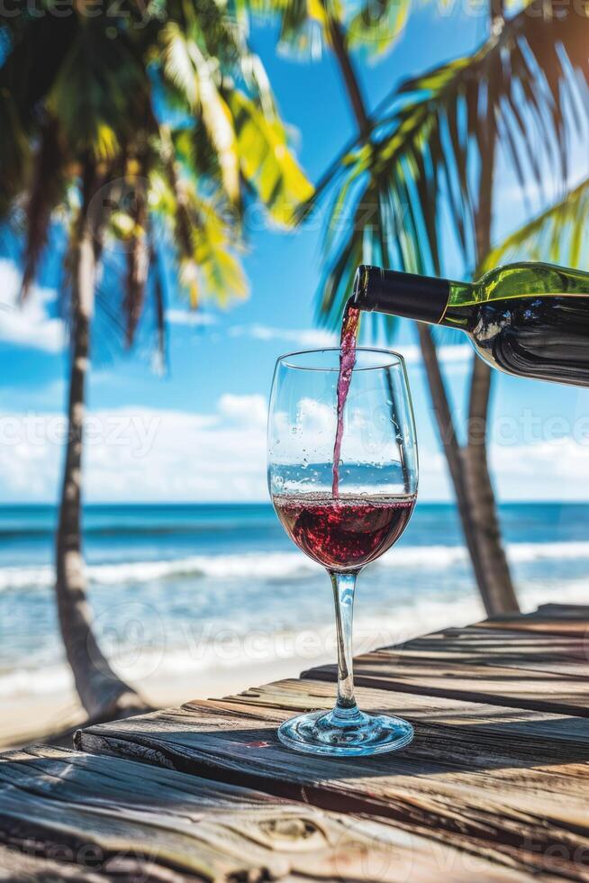 Pouring red wine into glass on wooden table at the tropical beach on a beautiful sunny summer day photo