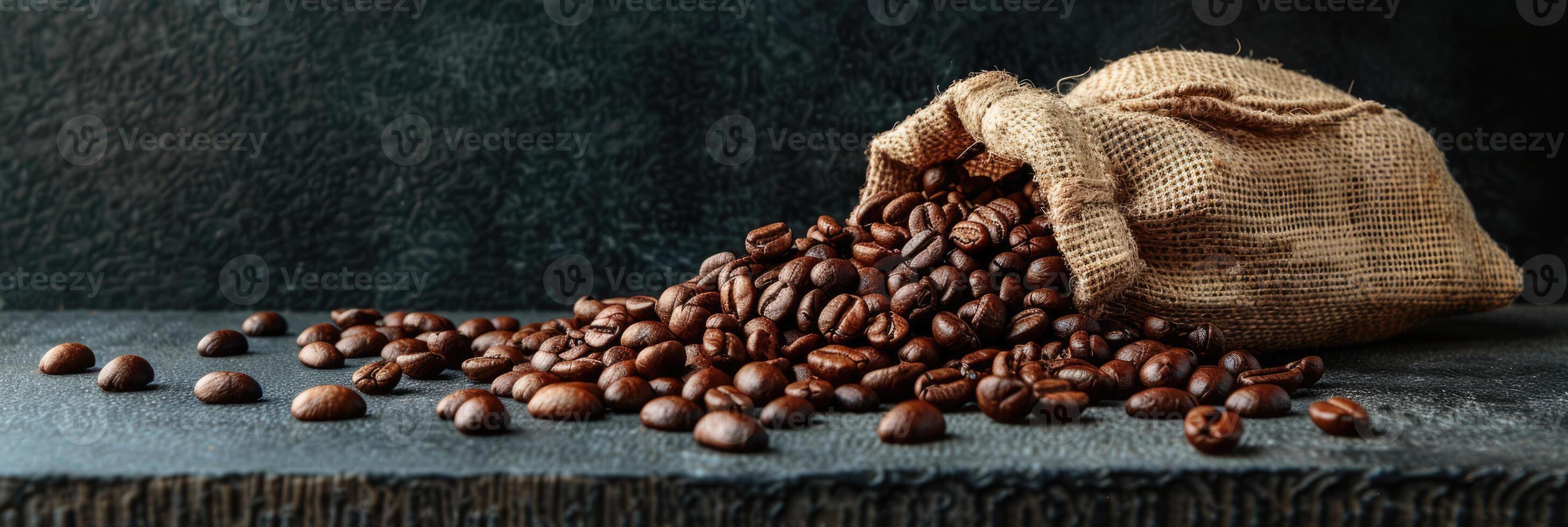 Roast coffee beans spilled out of a burlap sack onto a black table on dark background photo