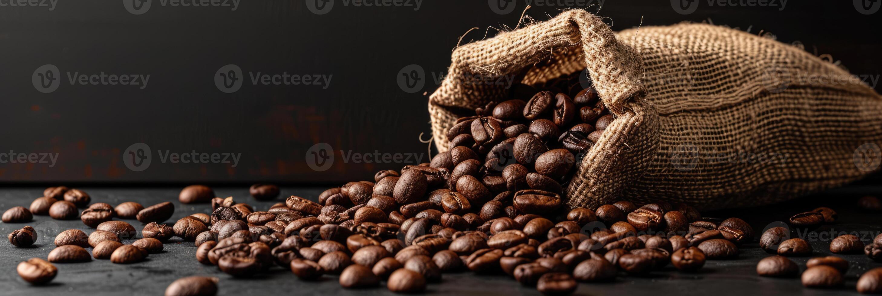 Roast coffee beans spilled out of a burlap sack onto a black table on dark background photo