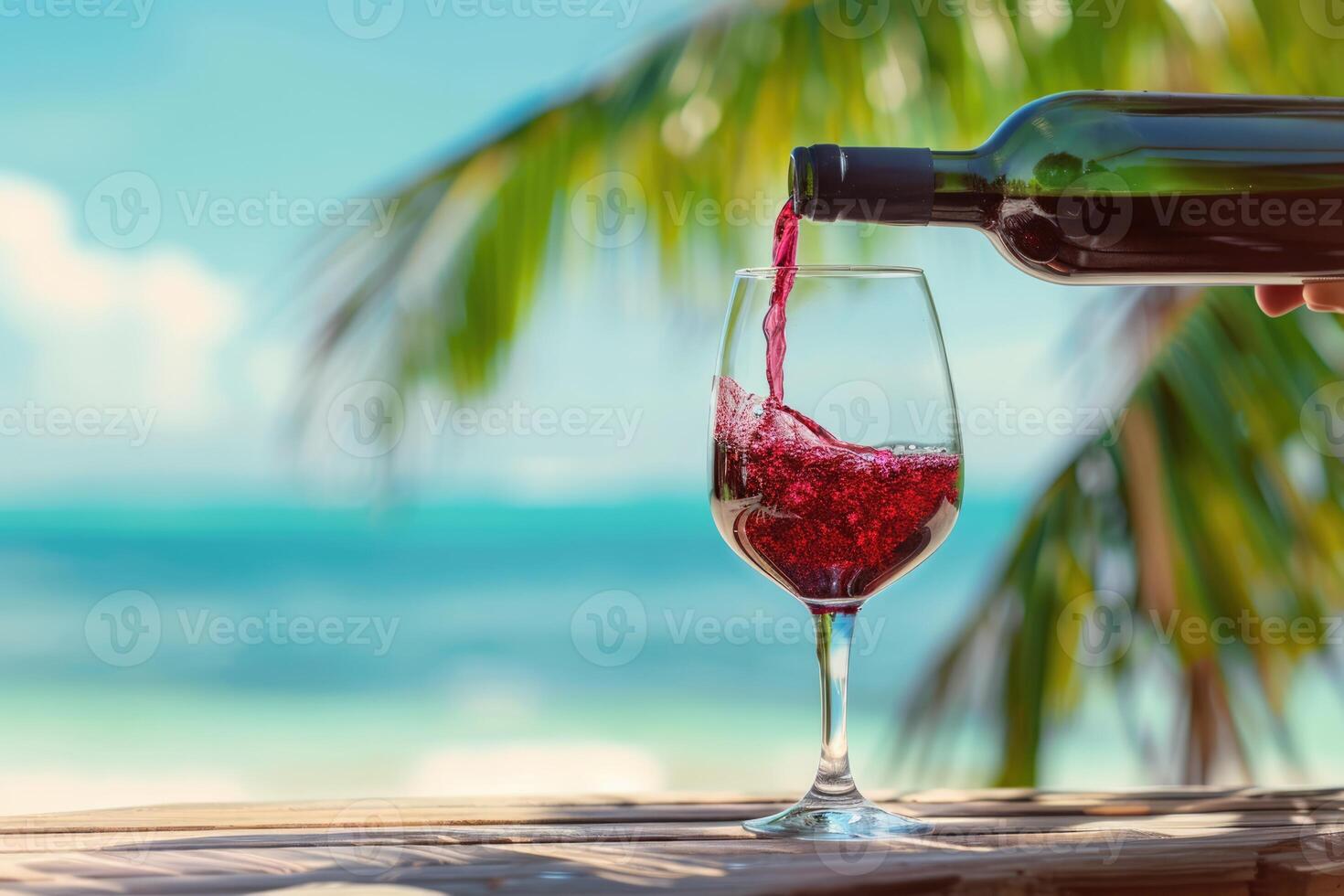 Pouring red wine into glass on wooden table at the tropical beach on a beautiful sunny summer day photo
