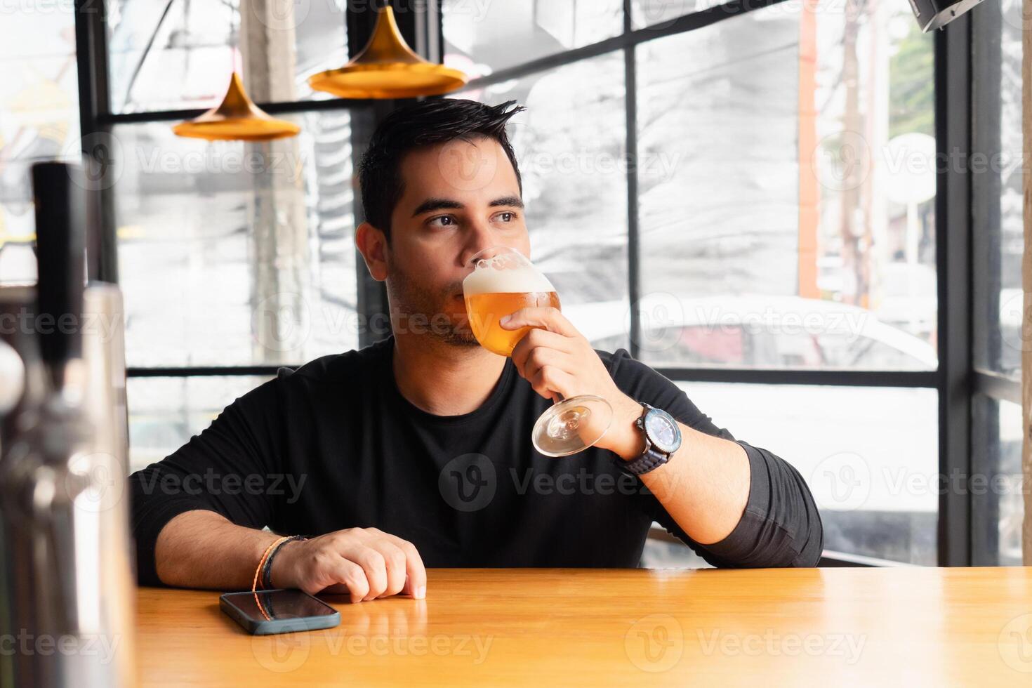 Latin man enjoying a refreshing lager beer in a chic, modern bar setting. photo