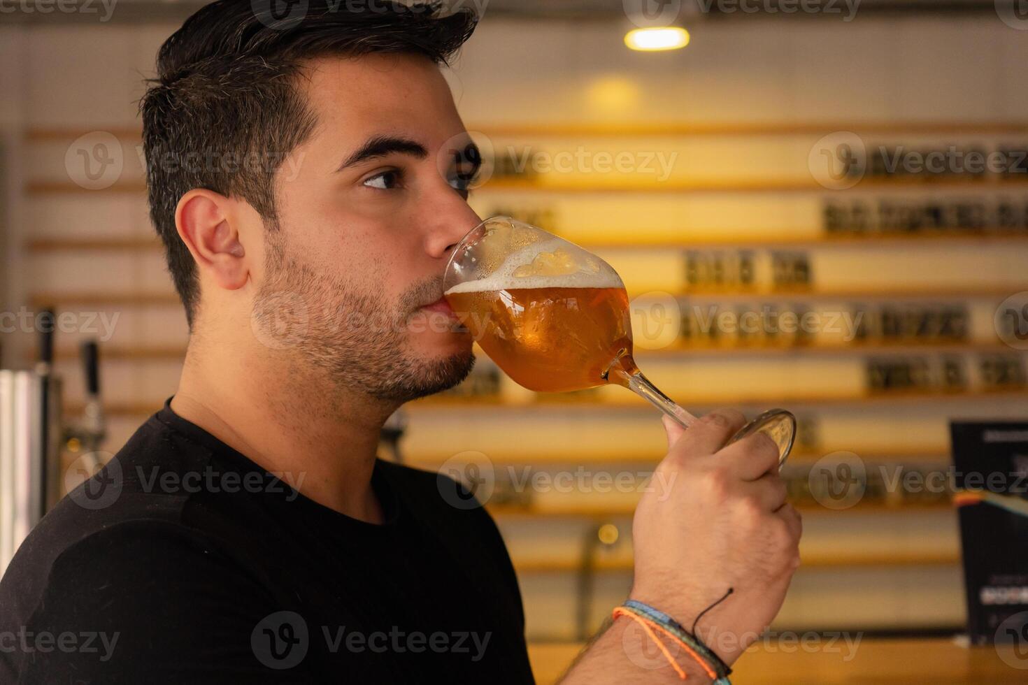 Close-up of young Latino man sipping a glass of beer in a pub. photo