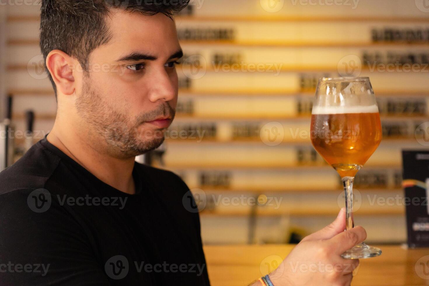 Young latin tasting craft beer in a pub, observing the color and hops in the lager. photo