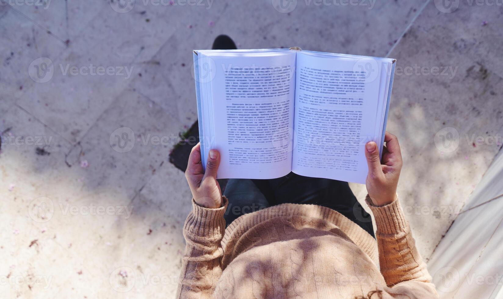 Person reading an open book outdoors, close-up view from above, enjoying a peaceful moment of study or leisure photo