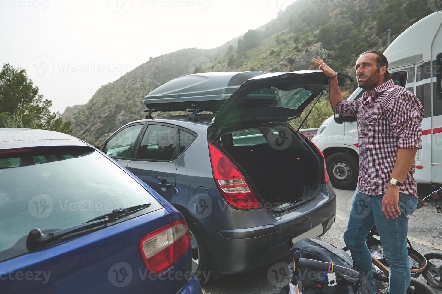 Man standing by car with open trunk preparing for outdoor adventure amidst scenic mountain landscape photo