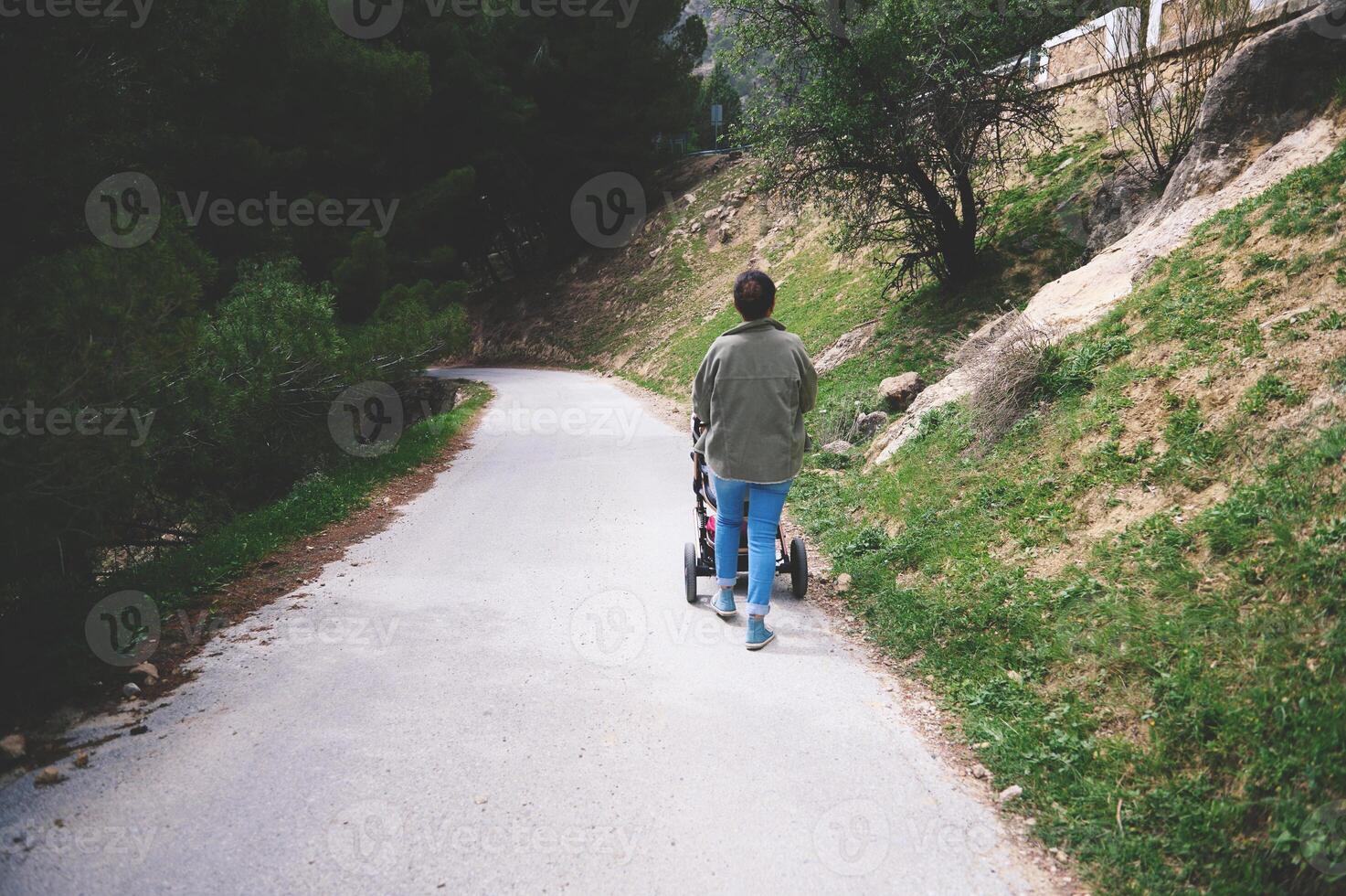 Person walking on a peaceful path in nature pushing a stroller, surrounded by trees and greenery photo