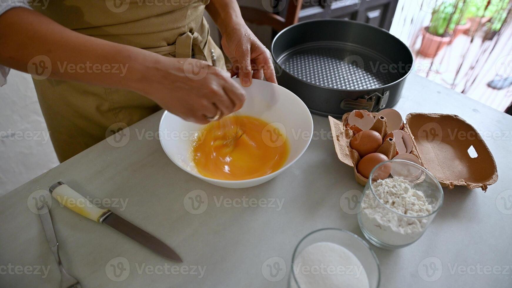 Person preparing apple pie batter with eggs, flour, and sugar in a kitchen photo