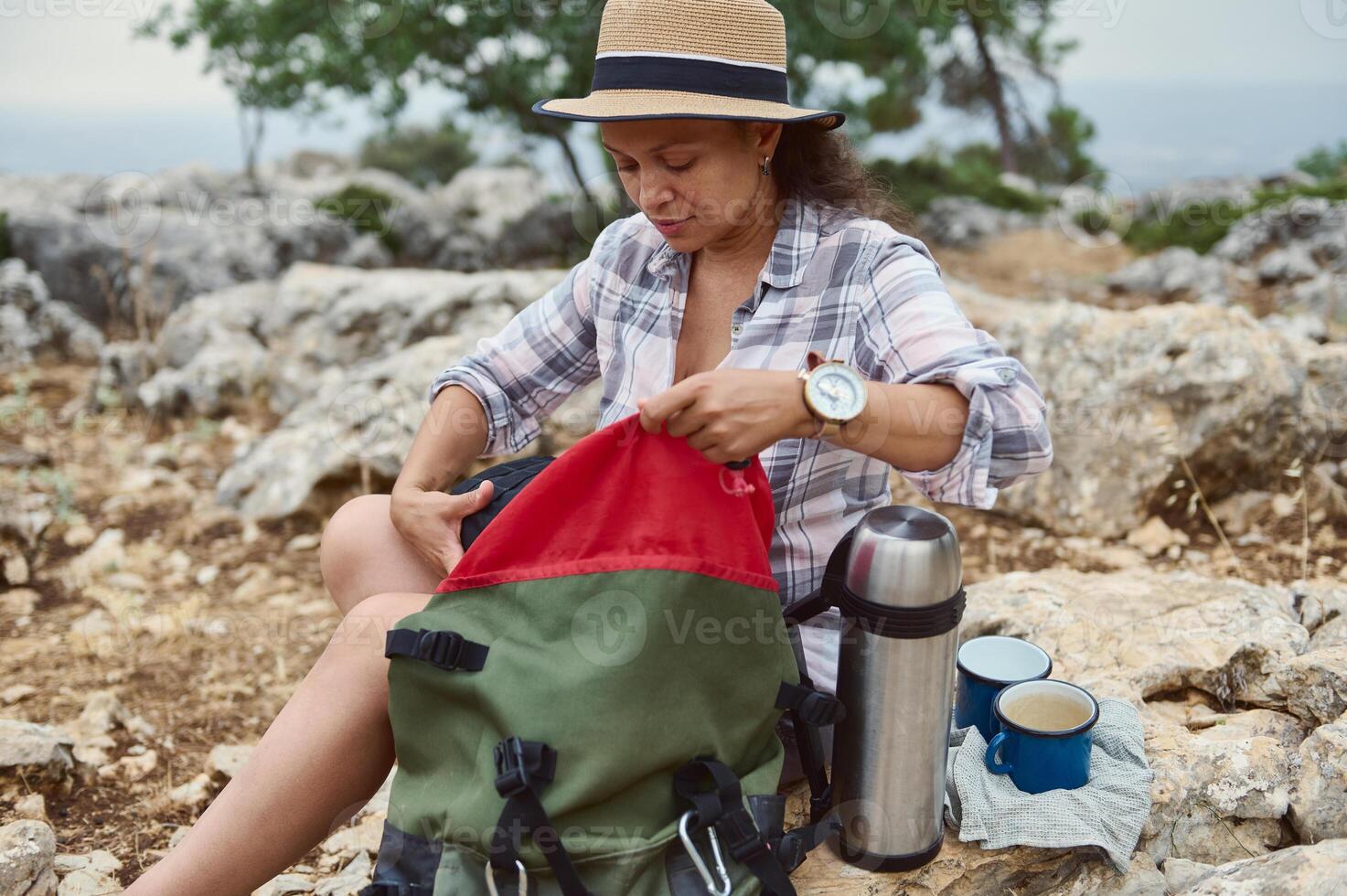 Woman packing backpack on rocky mountain trail during outdoor adventure photo