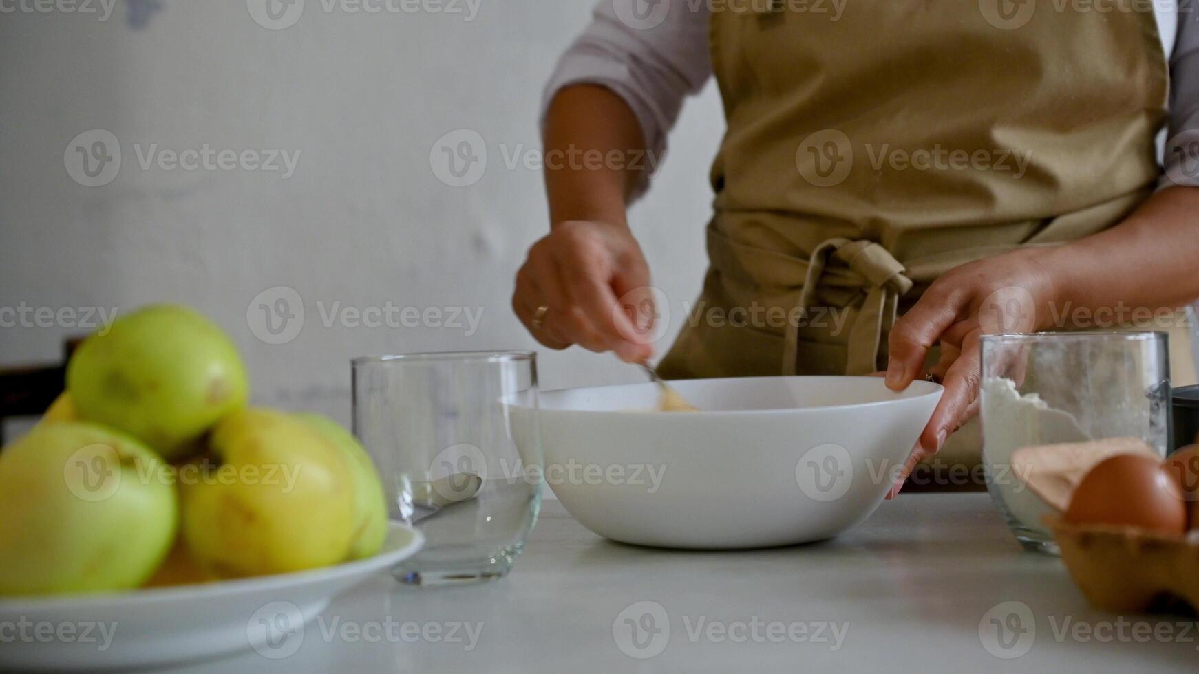 Baker mixing ingredients in a bowl with green apples, eggs, and flour on the table photo
