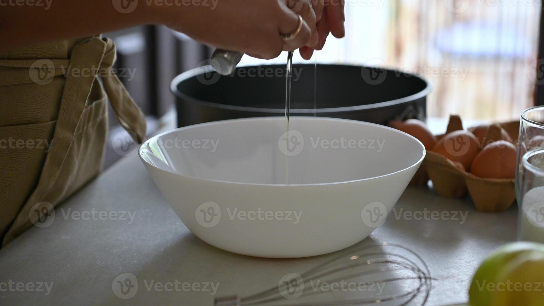 Person cracking an egg into a white bowl while baking in the kitchen photo