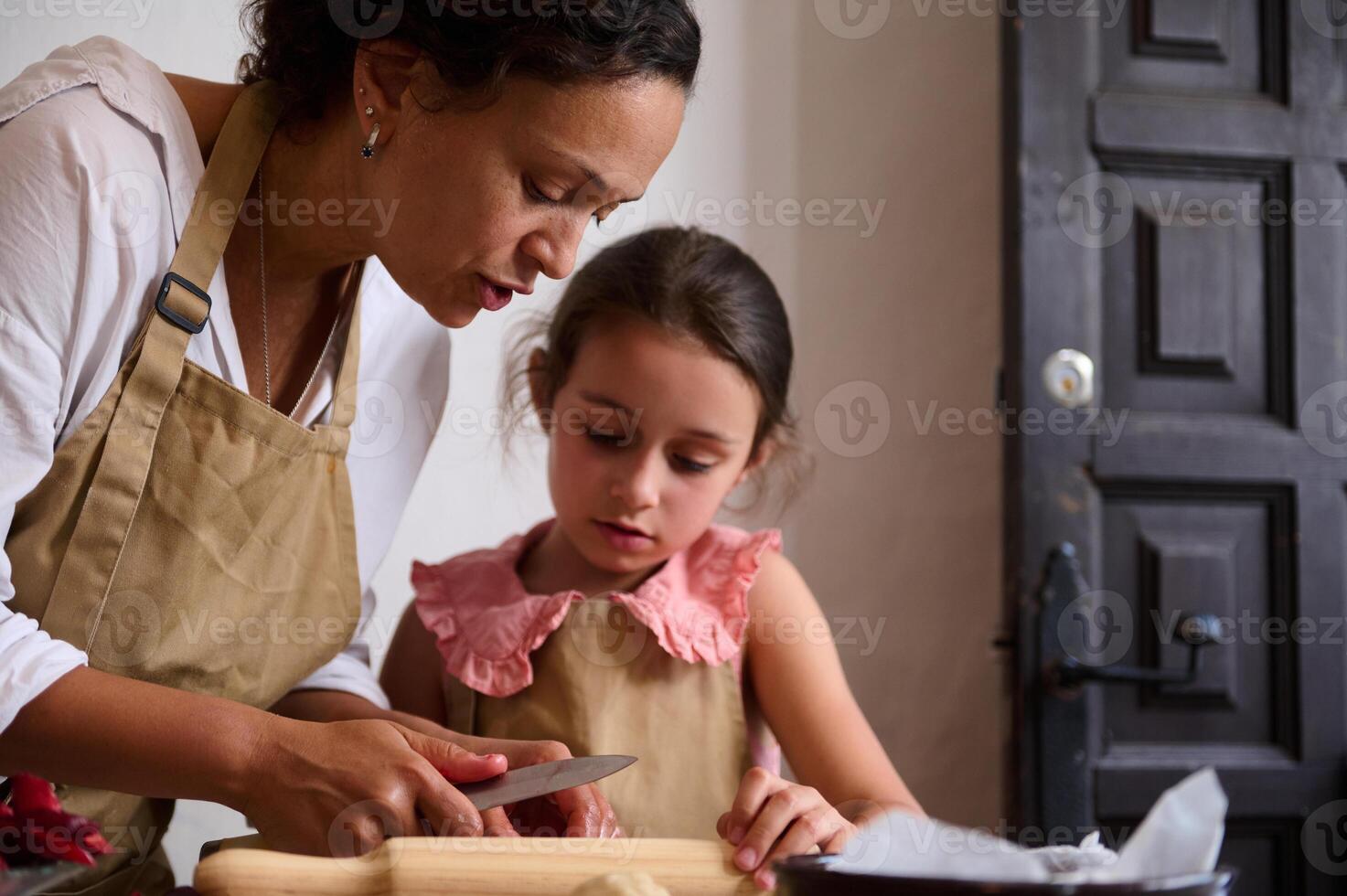 Mother and daughter wearing aprons cooking together in the kitchen photo