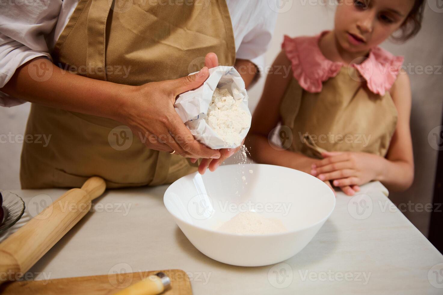 Mother and daughter baking together in the kitchen, pouring flour into a bowl photo