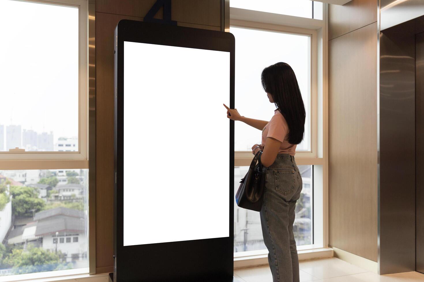 Woman using touch screen city display. Professional woman walking past a mockup display in a corporate hallway. photo