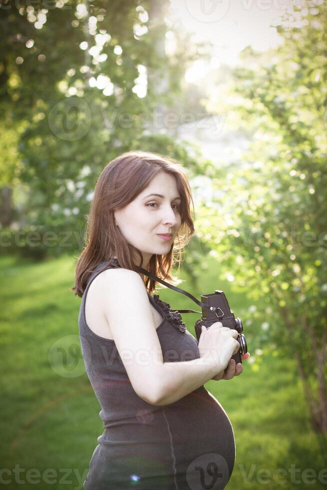 Pregnant woman with photo camera standing in park