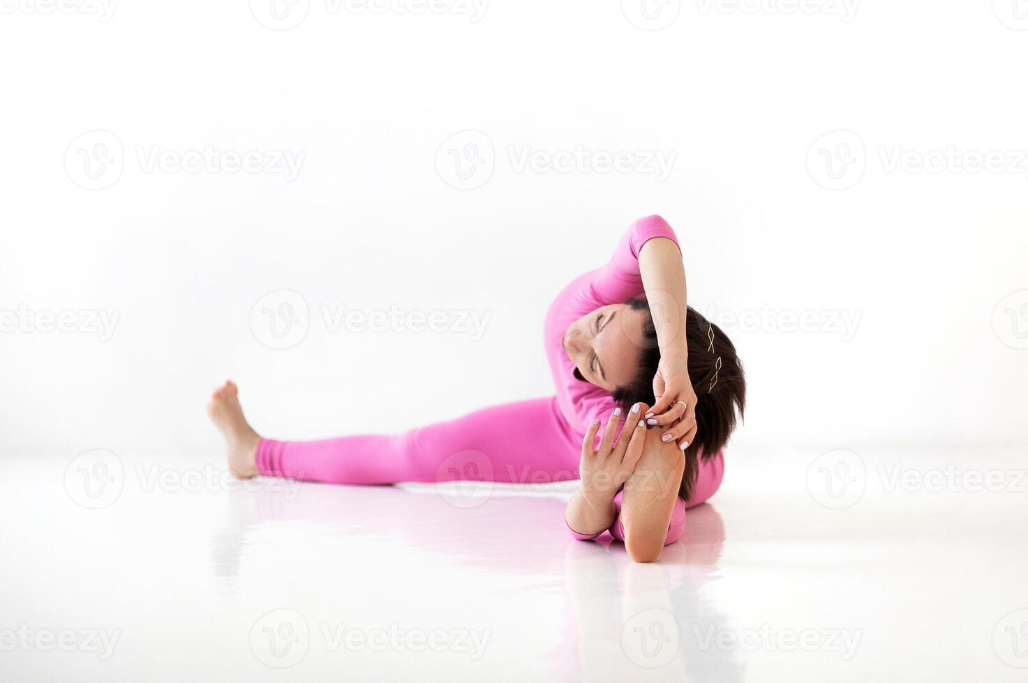 Young slender fit woman in pink long bodysuit performing yoga pose, isolated over white studio background photo