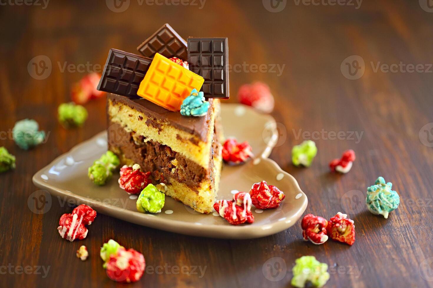 Piece of dark chocolate cake decorated with chocolate bars and pop corn on the plate photo