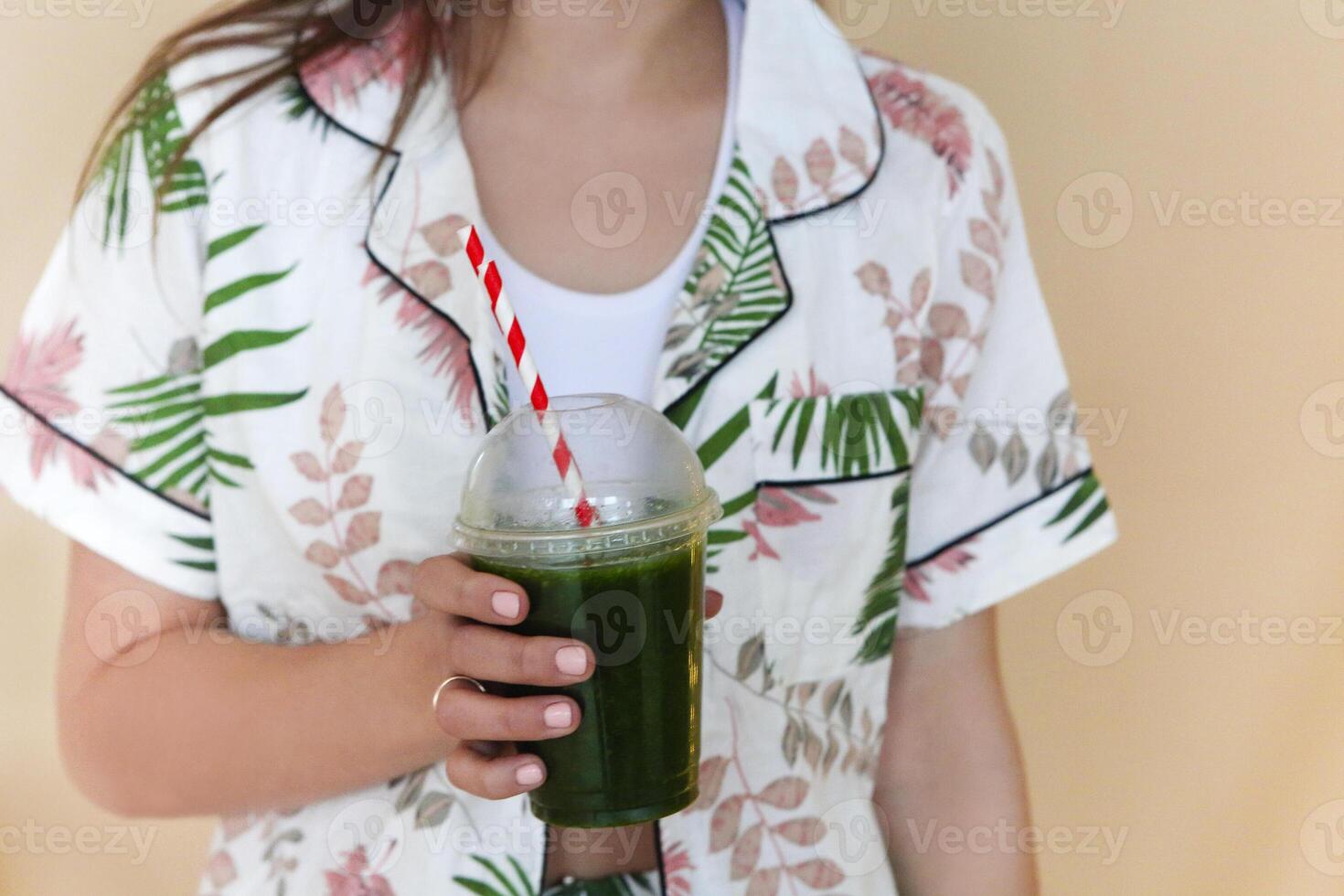 Delighted female with green smoothie laughing against wall background photo