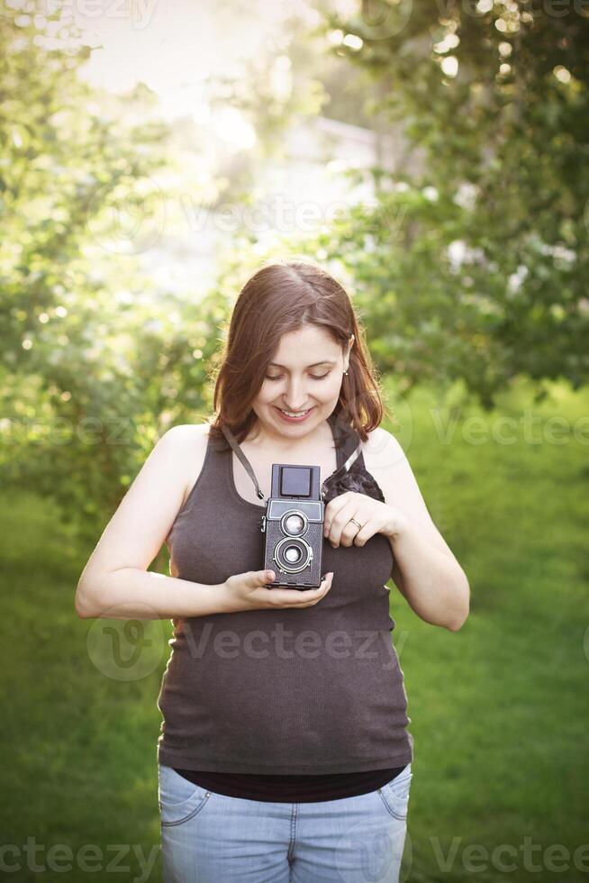 Pregnant woman with photo camera standing in park