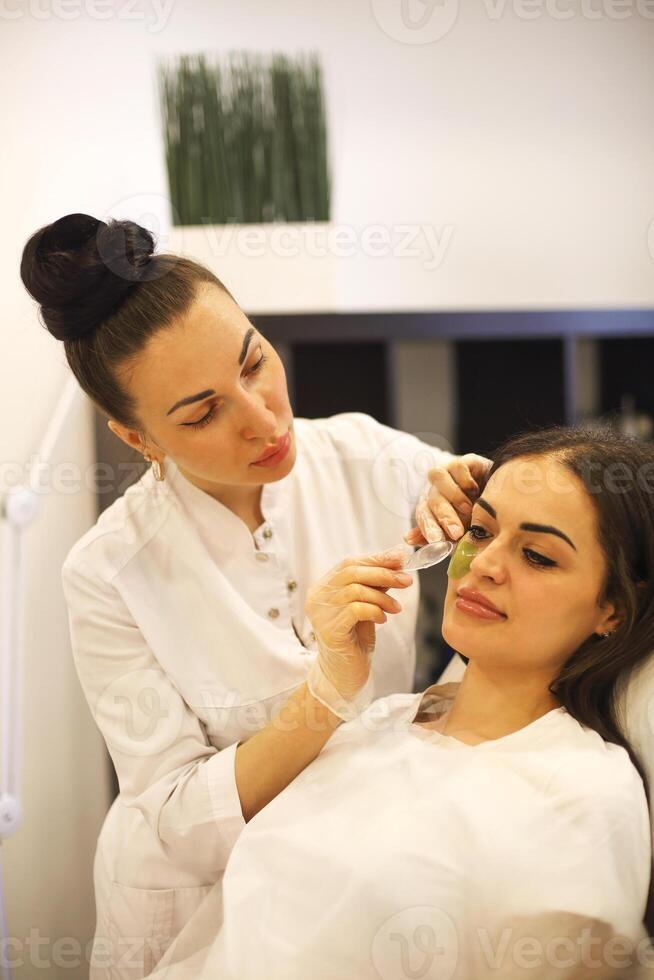 Cosmetician applying eye patches on face of woman photo