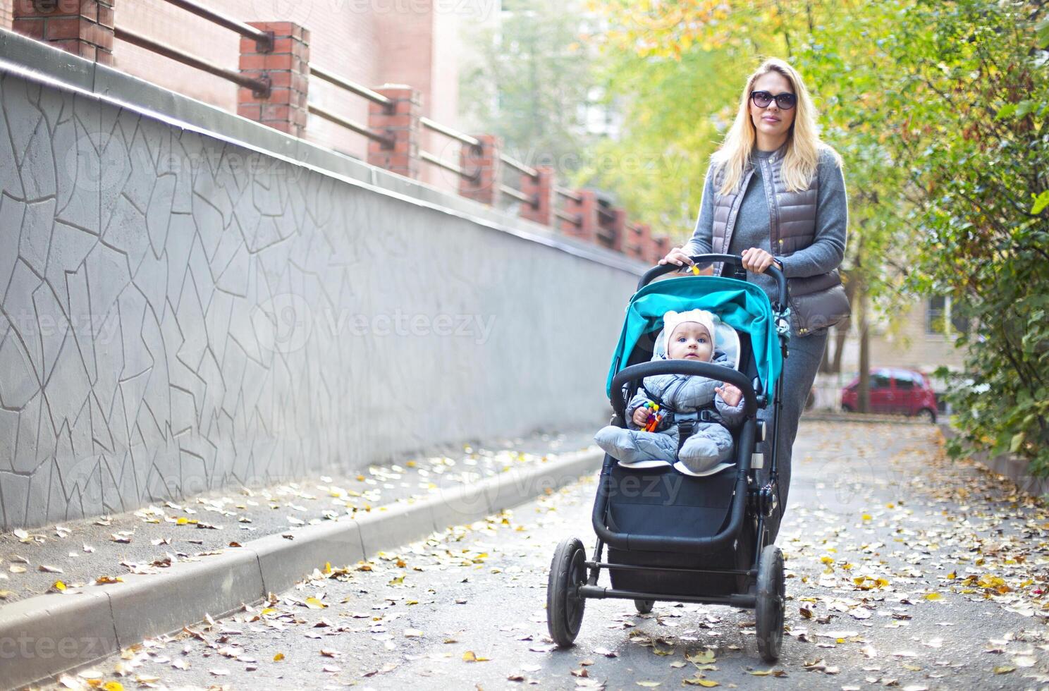 Young blond woman with stroller going for a walk in a park photo
