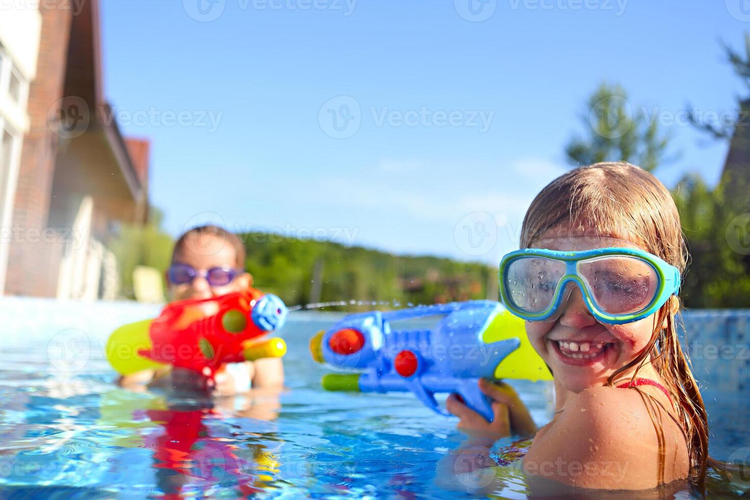 Funny little girls playing with water guns in the pool photo