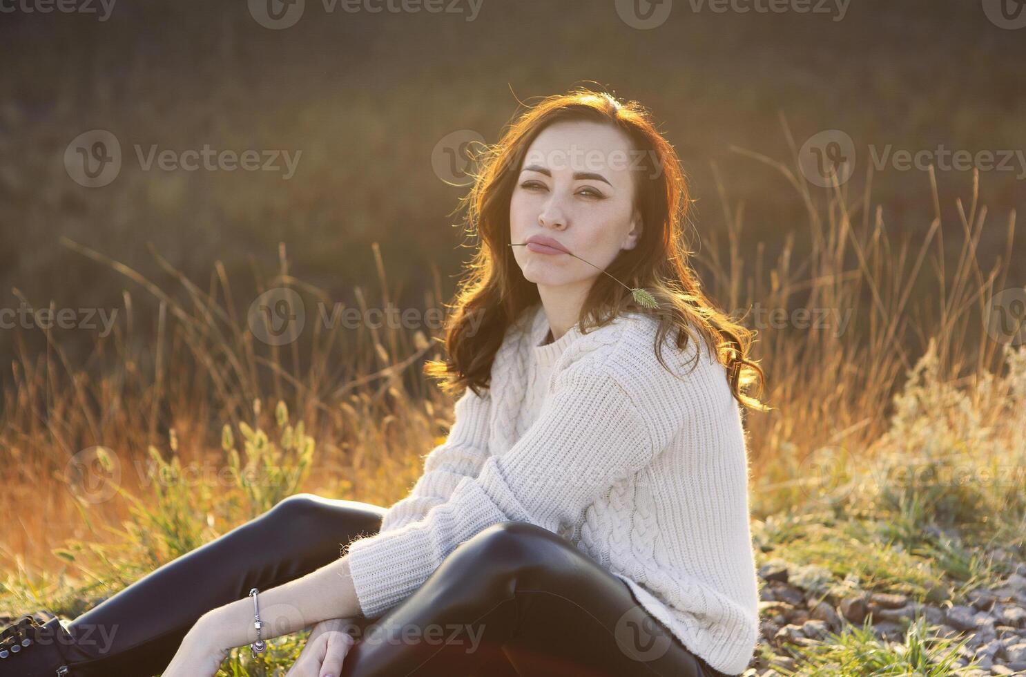 Young woman sitting in high grass at sunset photo