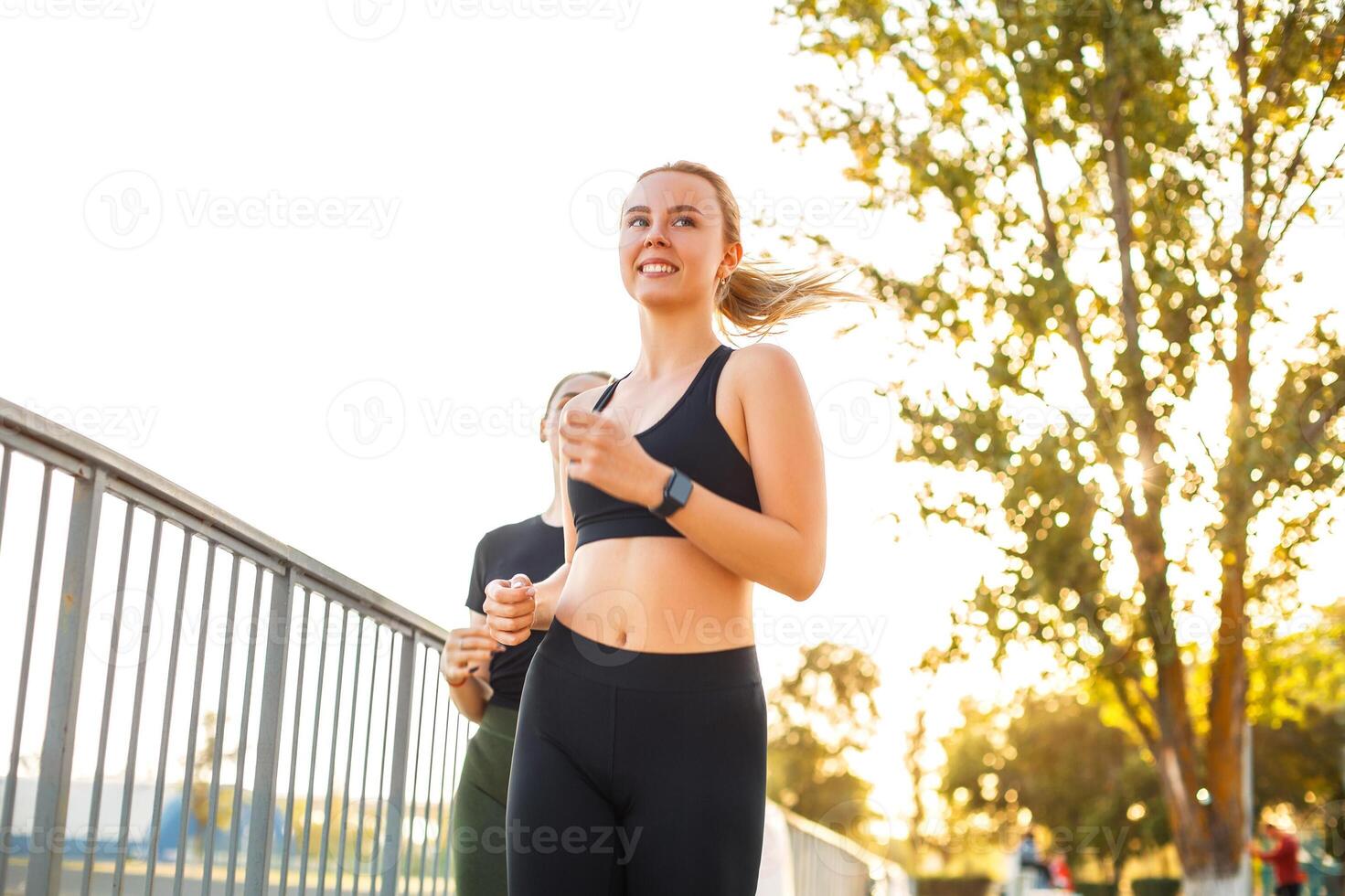 Two young sportive women runners in sportswear running together outside in public park photo