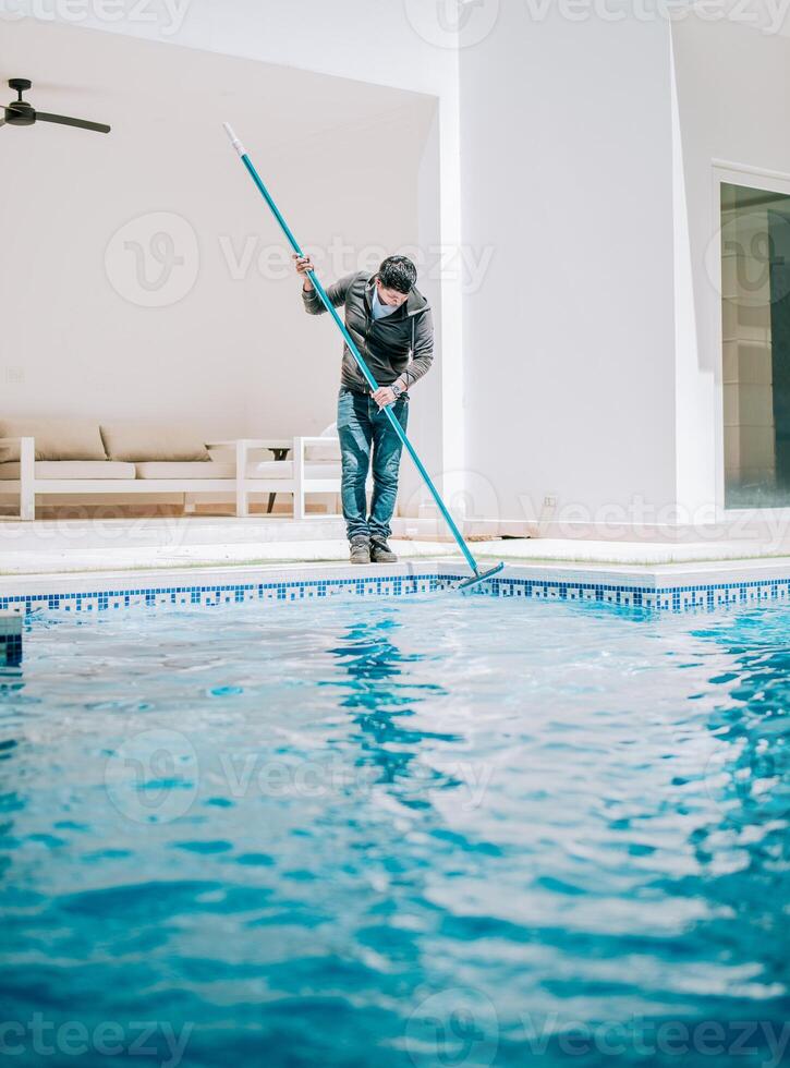 Male worker cleaning a home swimming pool with special brush. Home pool cleaning with wall brush photo