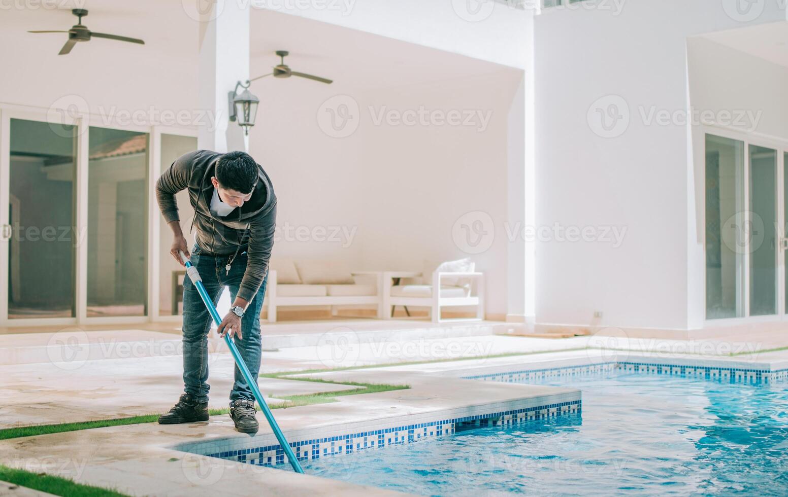 Worker cleaning a home pool with a vacuum hose. Man cleaning swimming pool with a suction hose photo