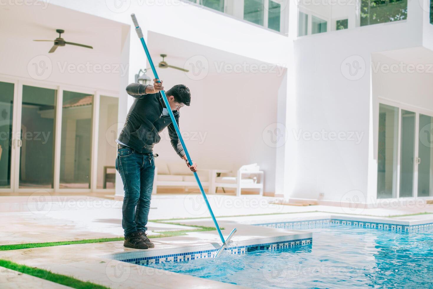 Person cleaning swimming pool with special brush. Maintenance person cleaning home pool with broom photo