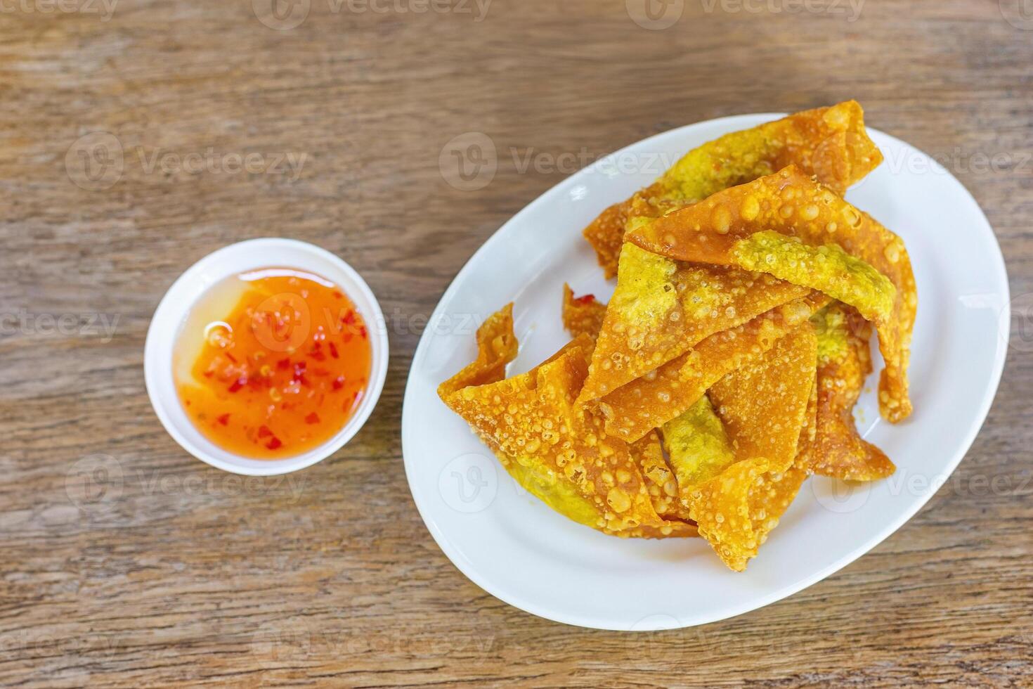 Delicious Thai style crispy homemade fried pork dumplings in a white ceramic plate with dipping sauce in a ceramic cup delicious Thai appetizers on a wooden table. photo