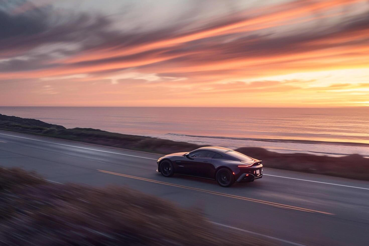 Prestige Luxury coupe cruising on coastal highway with the ocean stretching to the horizon and vibrant sunset sky photo
