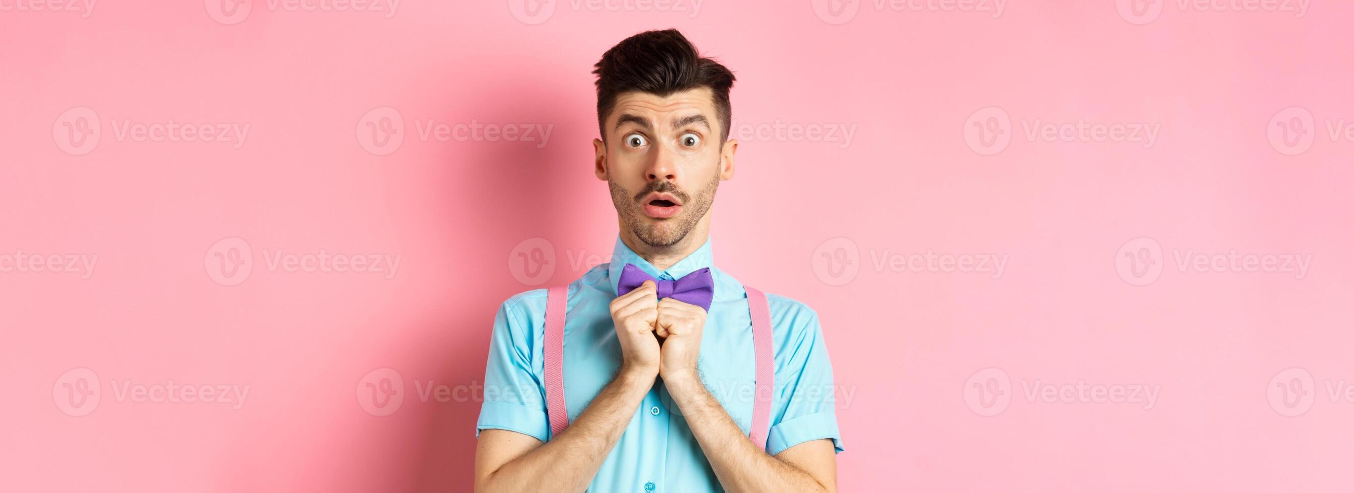 Startled and worried classy man in moustache, gasping and holding breath shocked, standing oin bow-tie over pink background photo