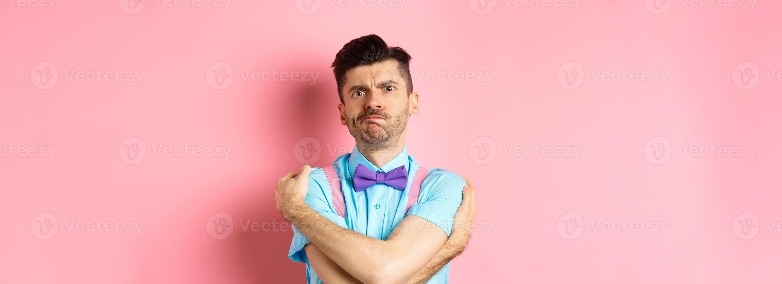 Timid guy embracing own body, comforting himself and looking offended, sulking at you, standing insulted and sad on pink background photo