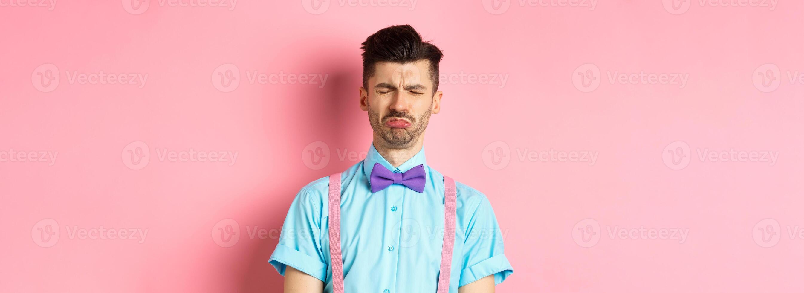 Sad and lonely man crying on valentines day, feeling lonely without lover, standing over pink background photo