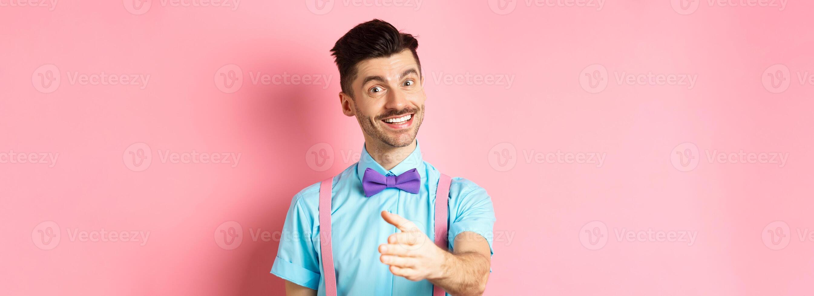 Nice to meet you. Handsome young man stretch out hand for handshake, smiling friendly and polite, introduce himself, standing over pink background photo