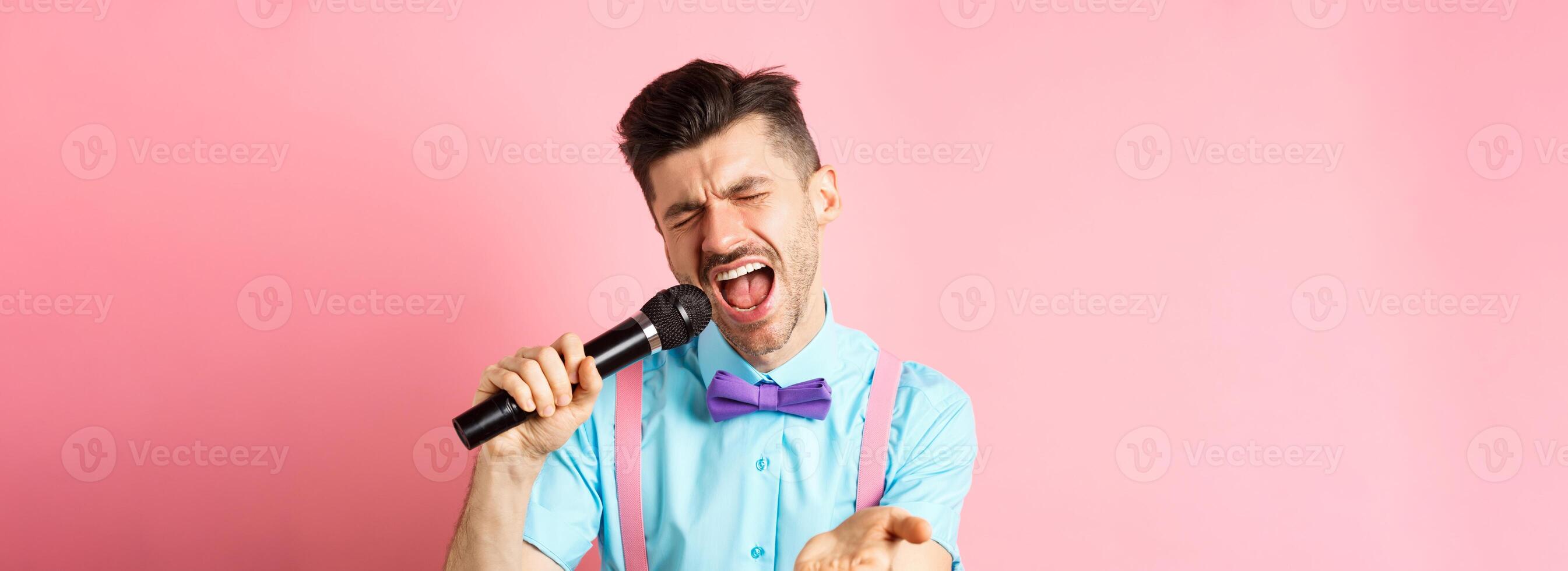 Party and festive events concept. Passionate singer holding microphone and pointing hand at you, singing about love, standing on pink background photo