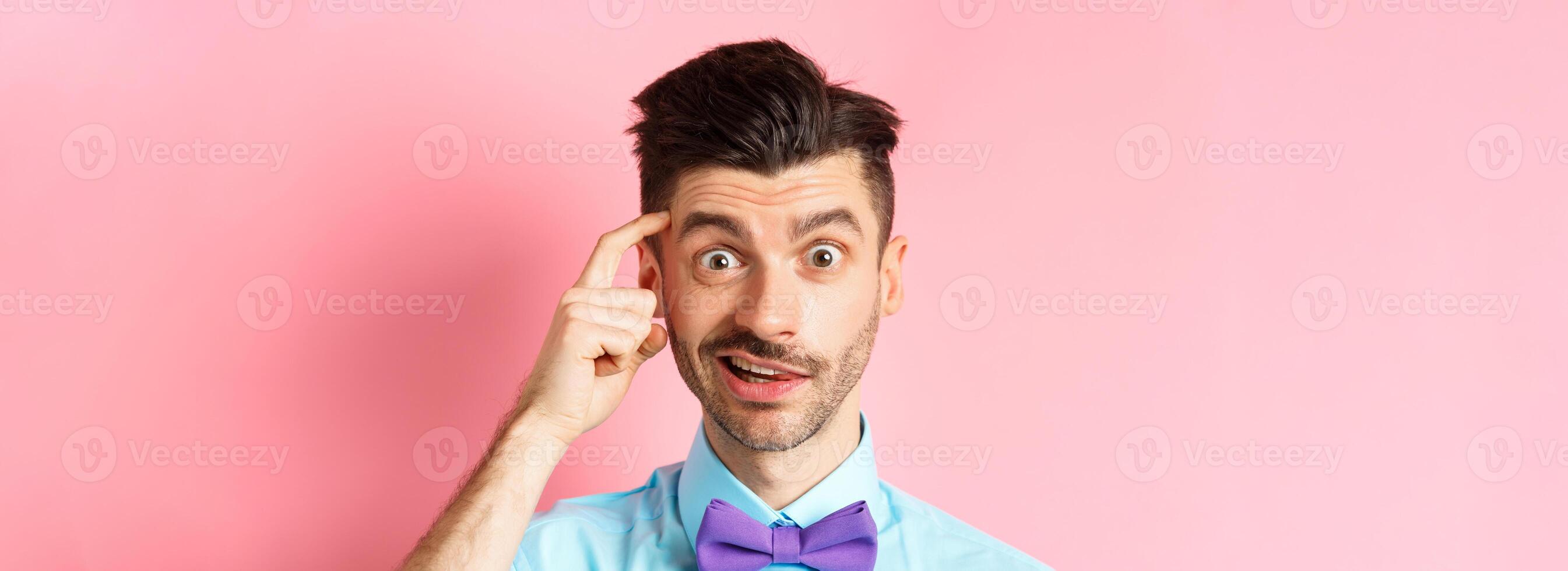 Close-up of confused guy in bow-tie, scratching head and looking puzzled, cant understand something, standing in bow-tie on pink background photo