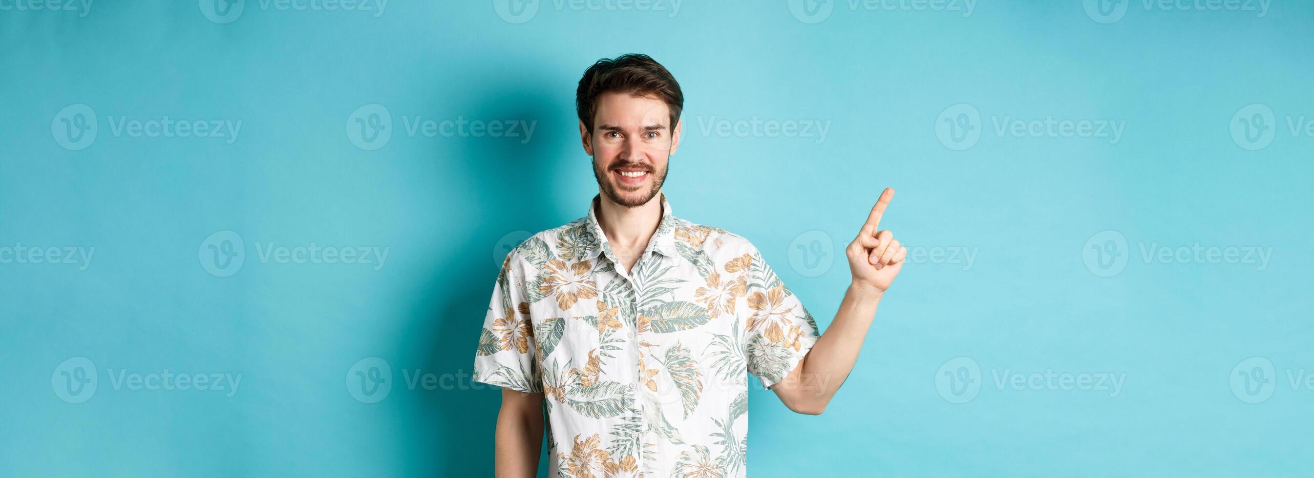Smiling tourist in hawaiian shirt pointing finger at empty space, showing logo. Concept of vacation and travelling photo