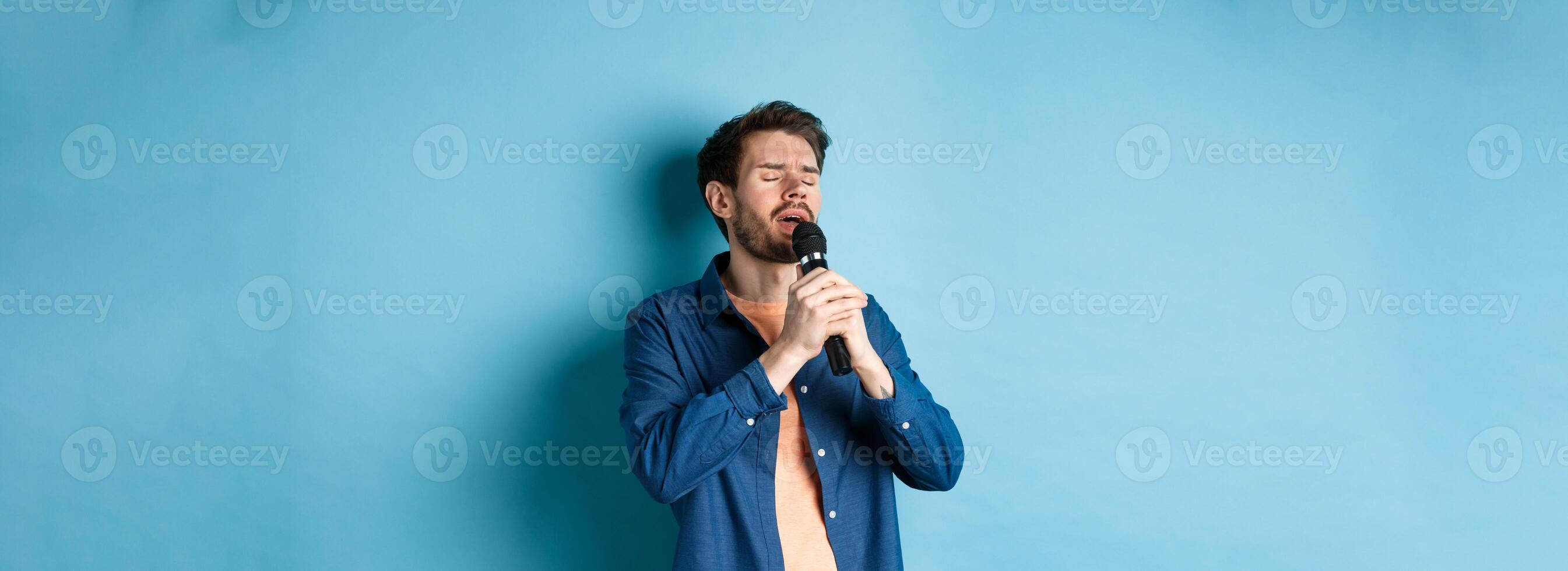 Romantic guy singing in microphone, performing on stage, standing on blue background photo