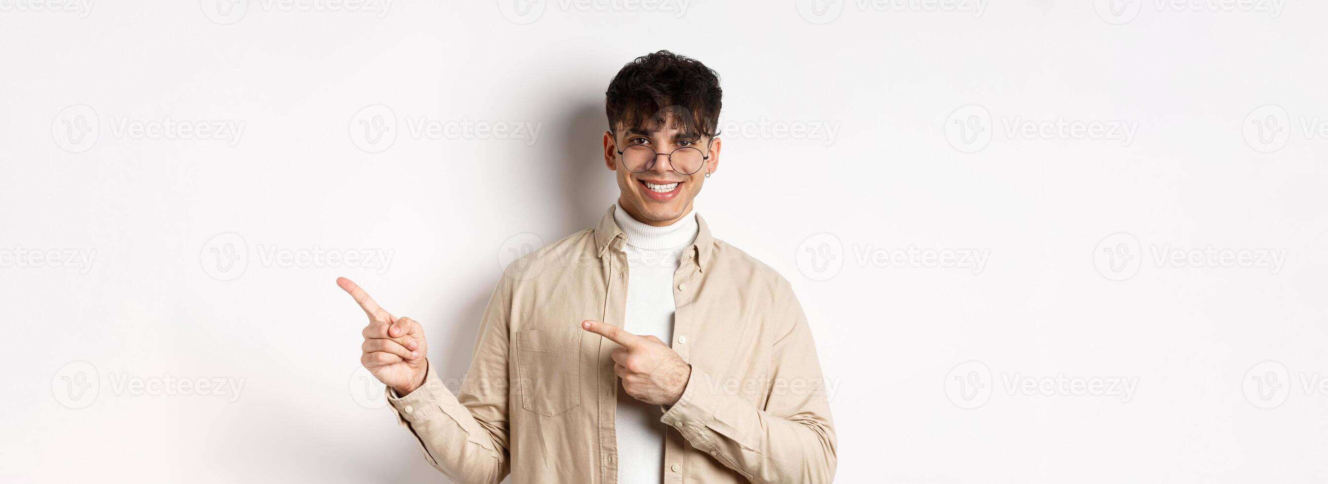 Handsome caucasian man in glasses smiling, pointing fingers at upper right corner, showing logo on white background photo