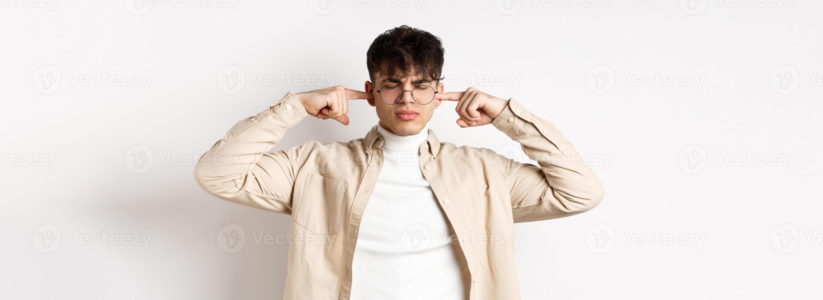 Annoyed young man shut his ears, block annoying sound, unwilling to listen, standing on white background photo