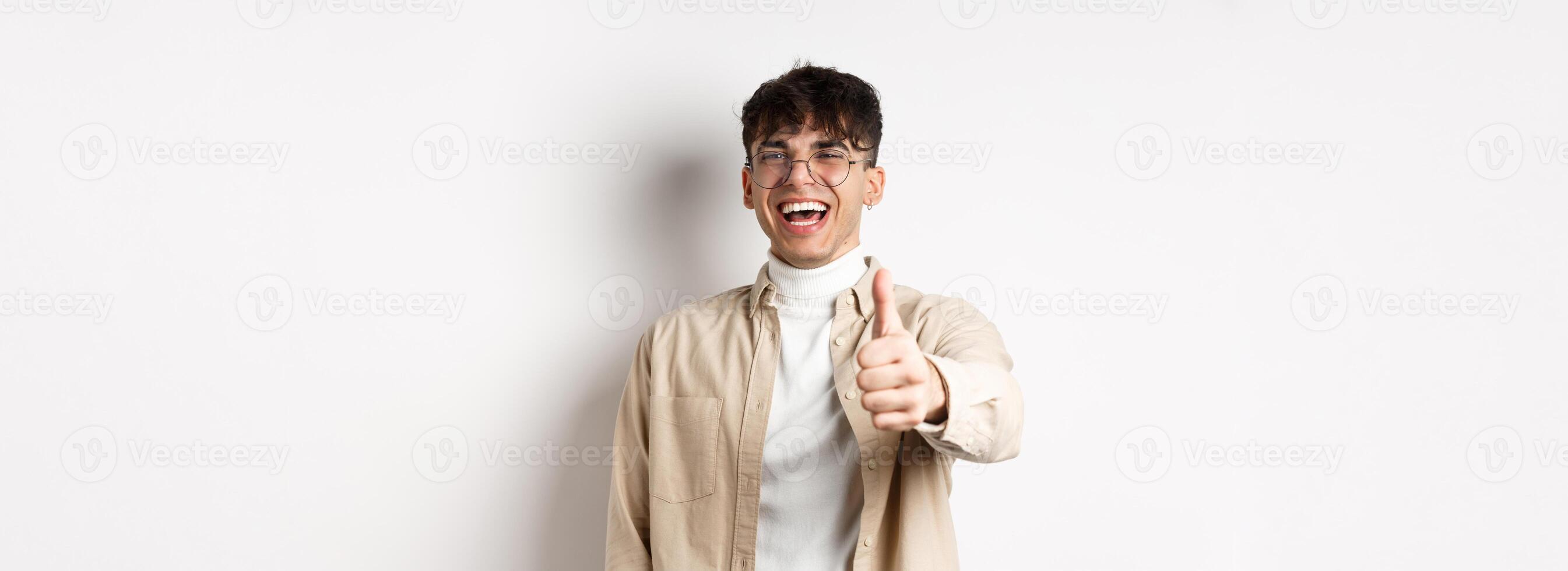 Nice one. Happy young man laughing and showing thumb up, like something good, standing on white background, complimenting you photo