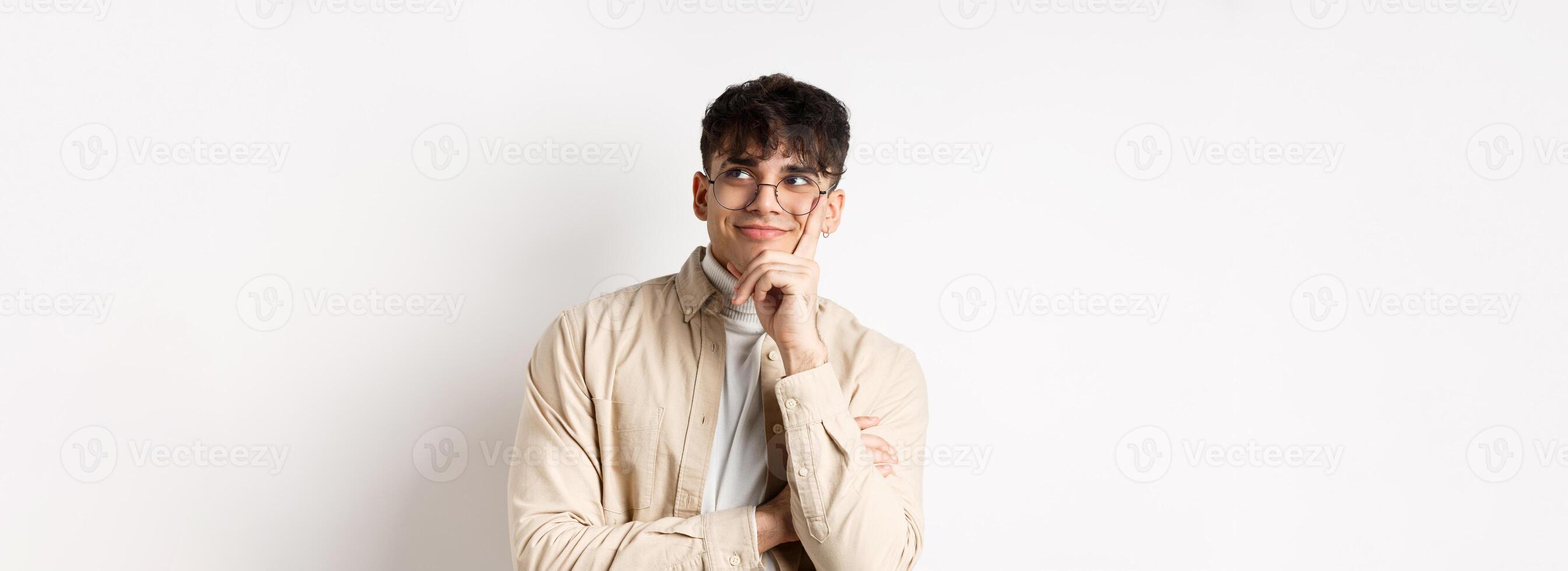 Image of happy dreamy young man imaging something good, smiling and looking at upper right corner thoughtful, standing on white background photo
