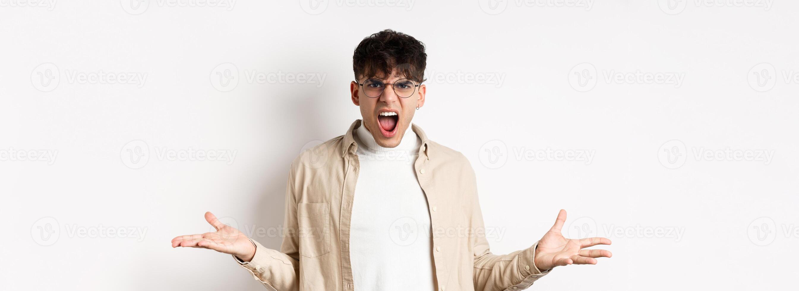 Portrait of angry frustrated man shouting and having argument, spread hands sideways and grimacing outrated, standing pissed-off on white background photo