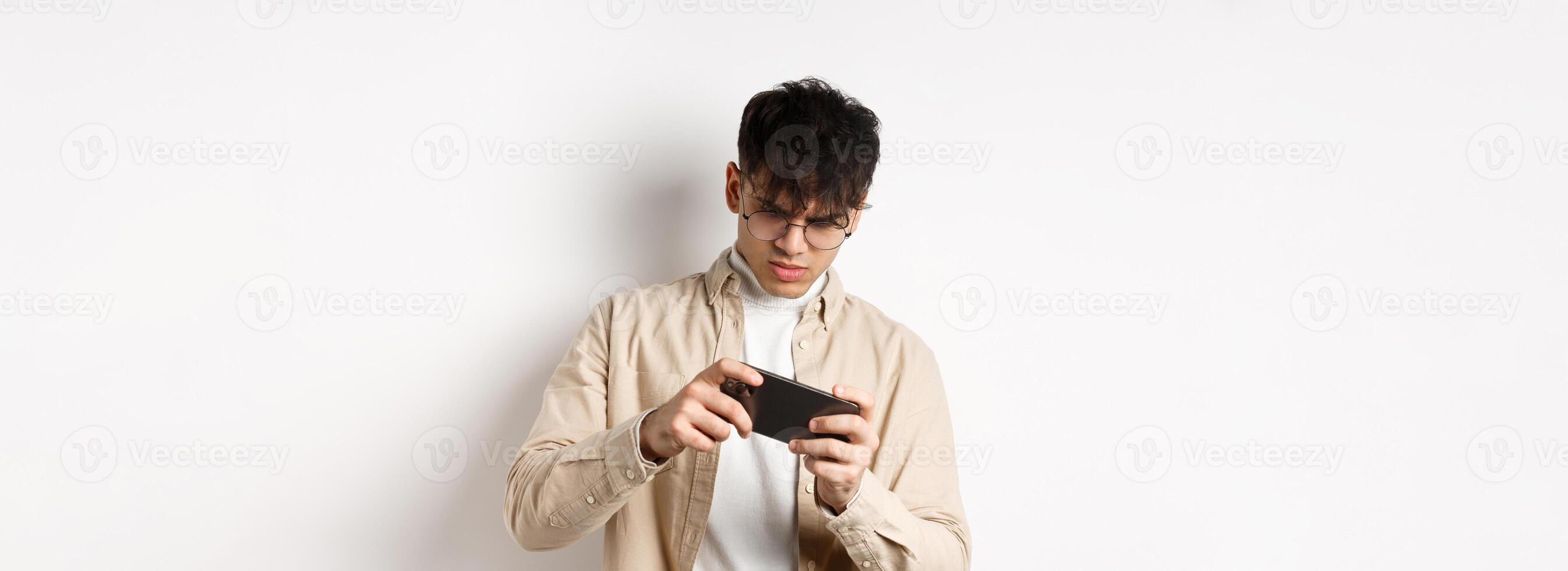 Portrait of handsome young man playing game on mobile phone, tilt smartphone to play racing, standing on white background photo