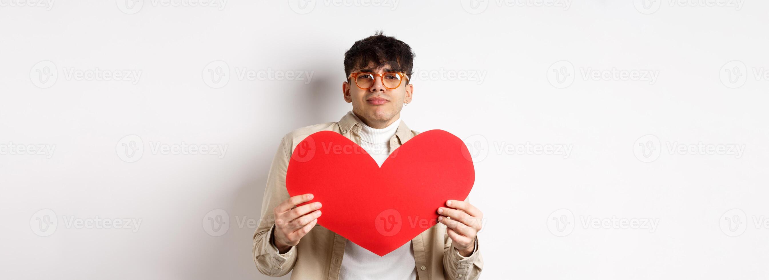 Passionate man waiting for lover with big red heart on Valentines day, looking romantic and with love, standing over white background photo