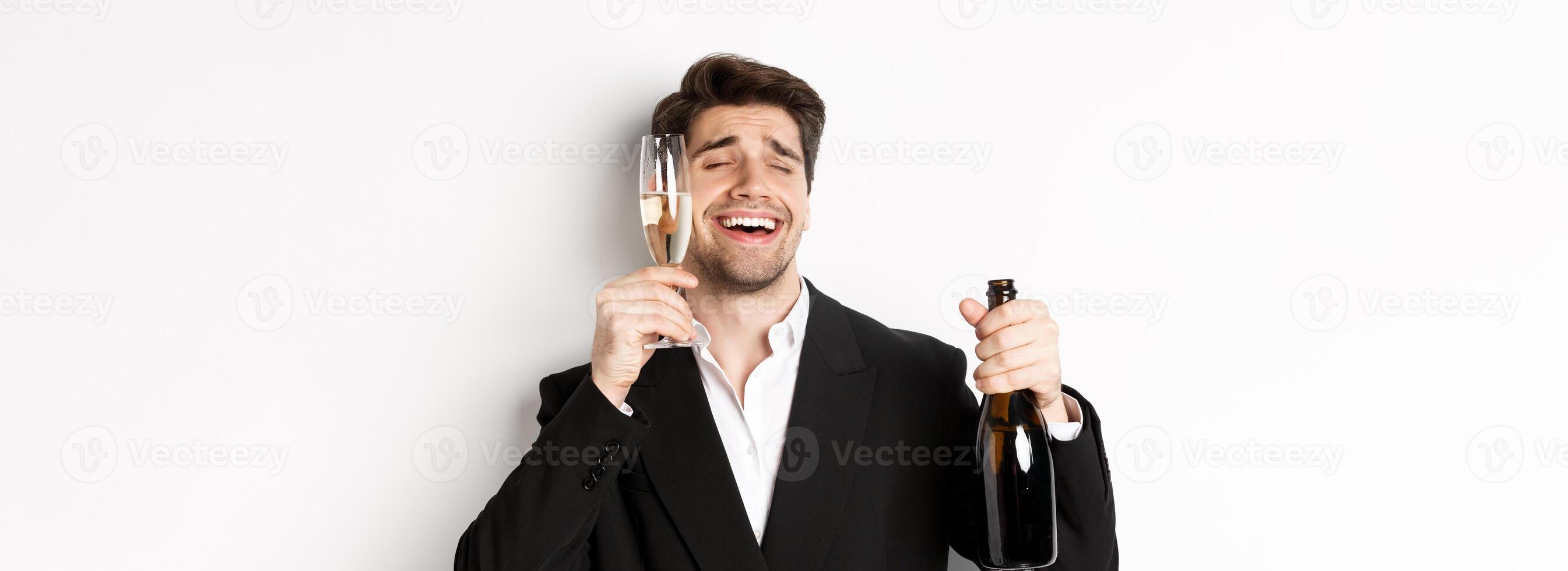 Close-up of handsome drunk guy in suit, holding glass of champagne and celebrating new year, standing over white background photo